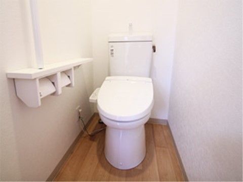 真っ白い壁と明るい色合いのフローリング調の床で清潔感のあるトイレ。シンプルなつくりだが、手摺もあり、立ち上がる時にも安心である。
