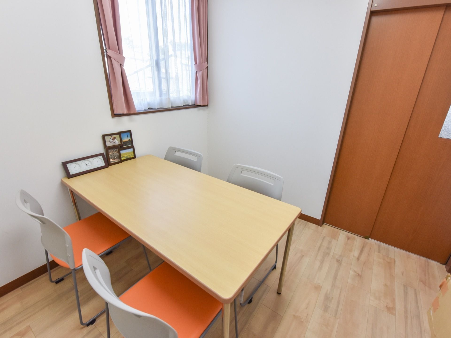 小窓の付いた部屋に、４人掛けのテーブルが設置されている。テーブルの上には時計と写真スタンドが置かれている。