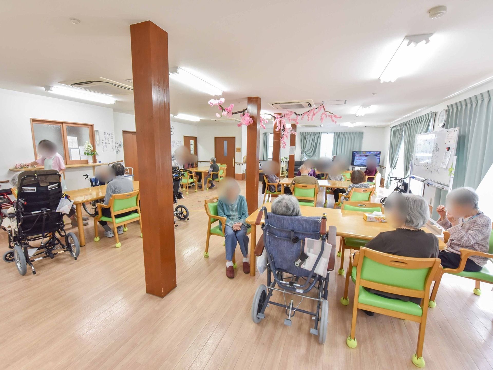 奥行きのある広々とした空間に、大きなテーブルが数個あり、各テーブルに6名程の入居者様が集まり談笑している。