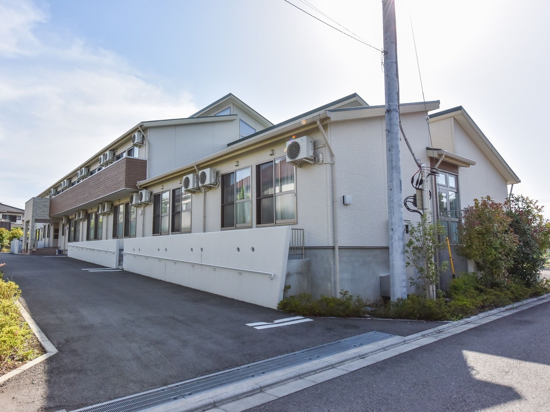 建物の周りには植栽が施されている。道路から入口へは緩い勾配の坂になっている。窓の外にはエアコンの室外機がある。