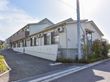 建物の周りには植栽が施されている。道路から入口へは緩い勾配の坂になっている。窓の外にはエアコンの室外機がある。