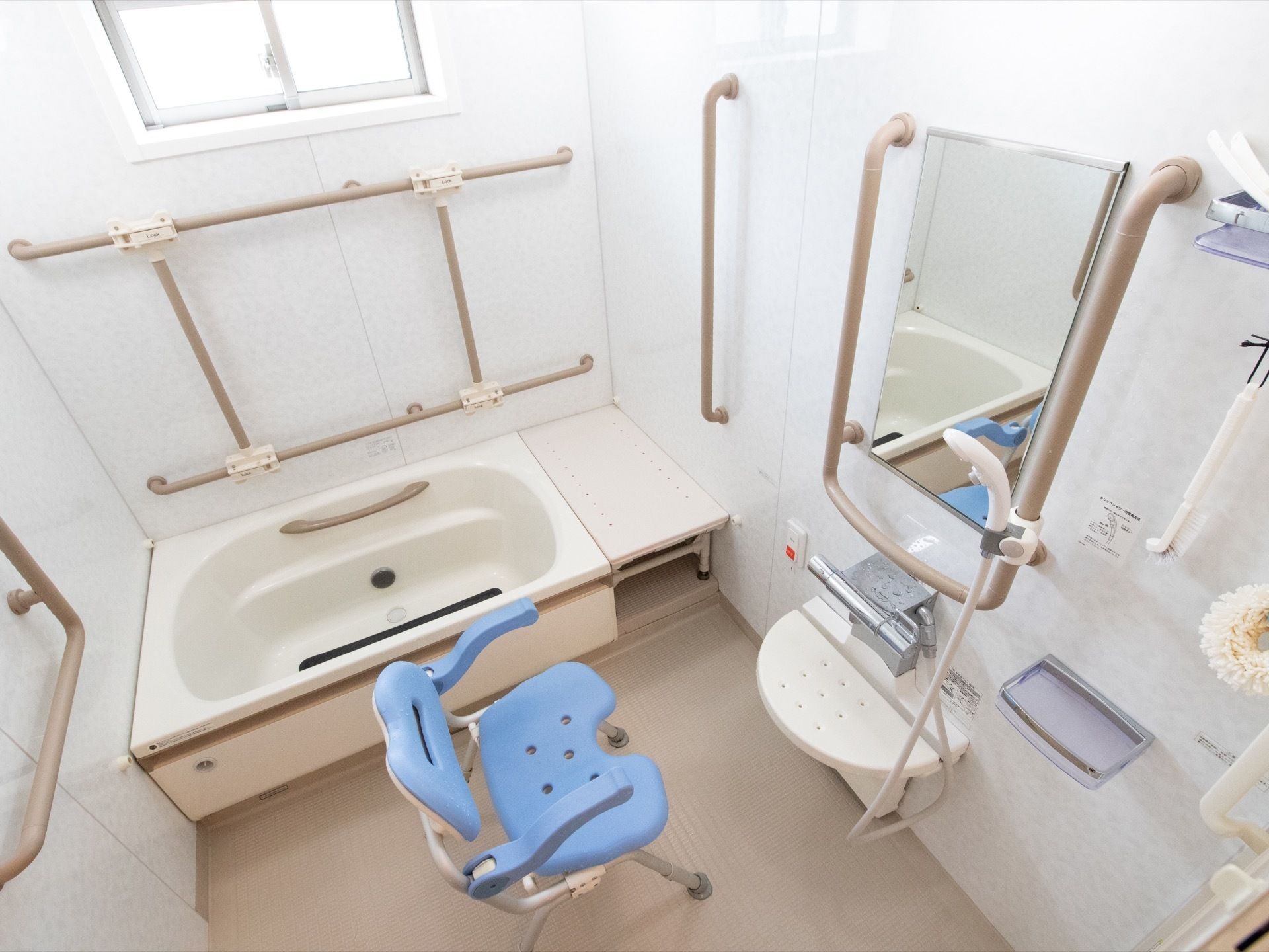 壁には複数の茶色い手すりがついており、シャワーチェアが置かれている。浴槽側の壁の上には小さい窓がある。