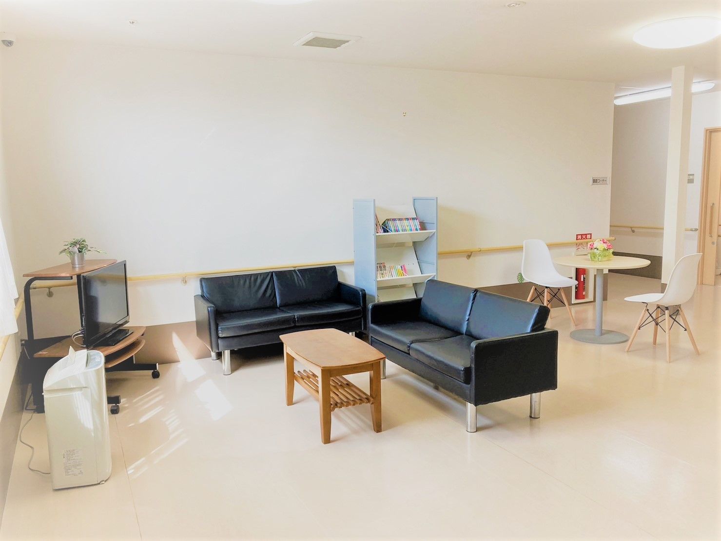 部屋の中心には細い柱が立っており、茶色いソファとテーブルが置かれている。壁には手すりが備えてあり、時計が掛けられている。