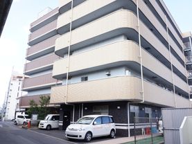 施設の一階部分に駐車場があり、車が数台停めてある。玄関の周りは、フェンスがあり、木が植栽してある。ベランダがついた建物である。