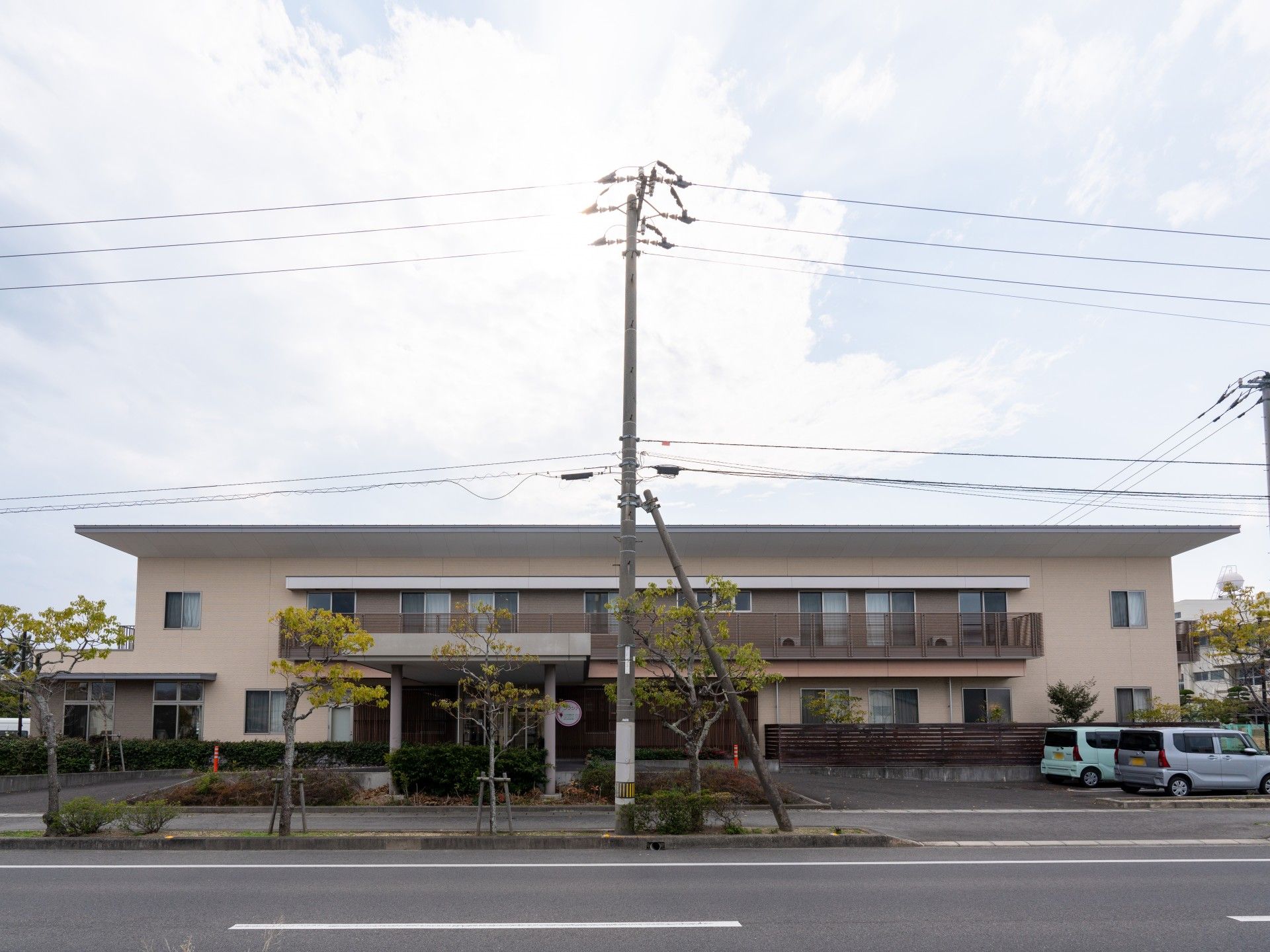 玄関前に樹木が植えられていて、車寄せがある窓が多い二階建ての建物