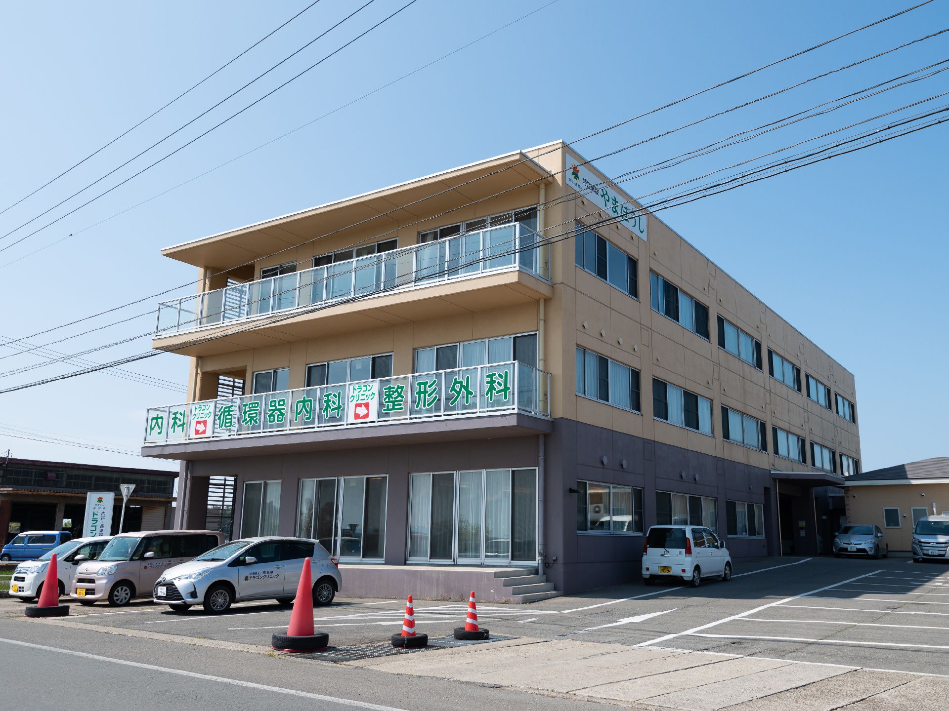 駐車場が広く車が数台停まっている、ベランダ付三階建ての建物