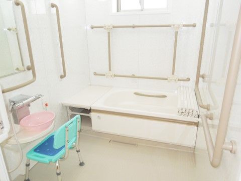 手すりがたくさん設置されていて、水色の椅子が置いてある白い浴室