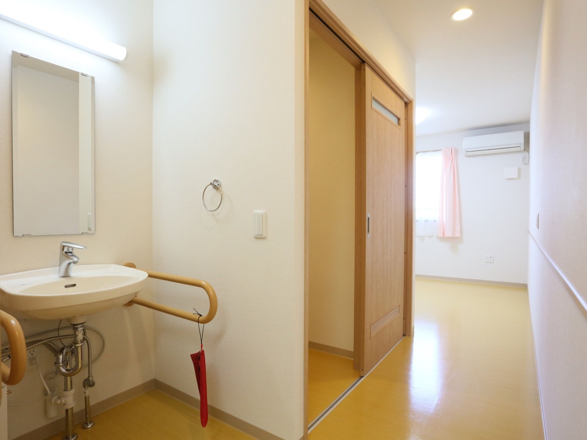 居室に完備された洗面台の両サイドに、木製の手すりが設置されている。縦長の鏡、上部には横長の照明が備えつけてある。