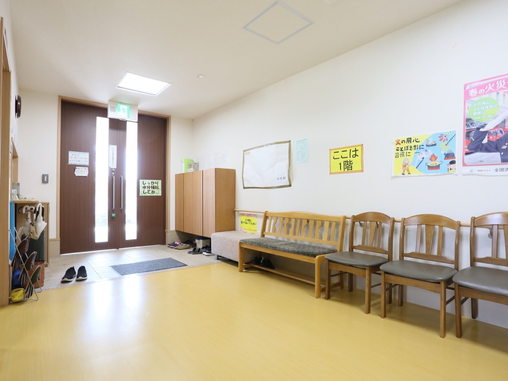 壁に沿って靴箱と椅子が数脚置いてある両開きドアのエントランス