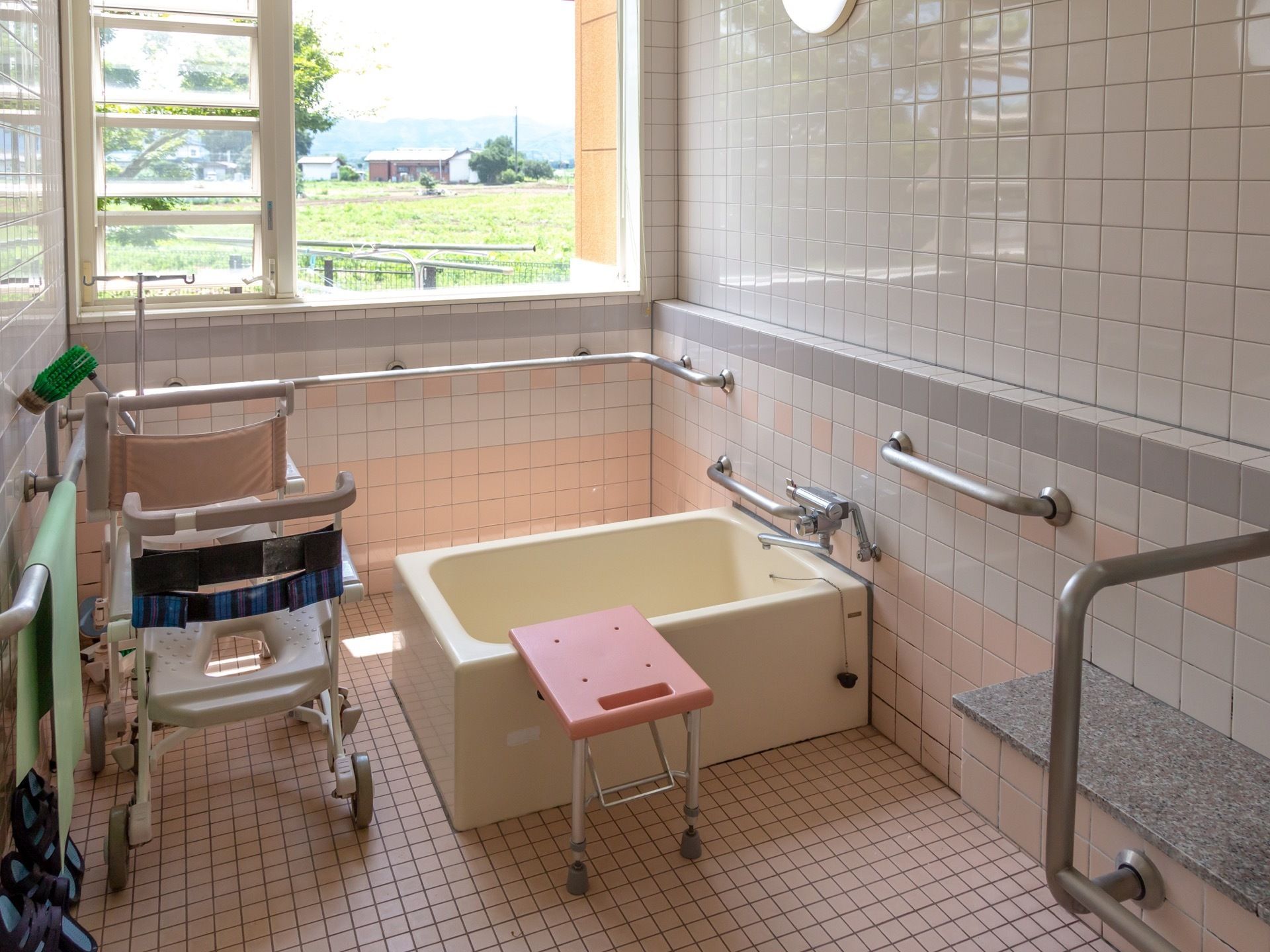 個浴用浴室の壁には手すりが取りつけられている。浴室用車椅子が置かれ、浴槽のへりに腰掛が設置されている。
