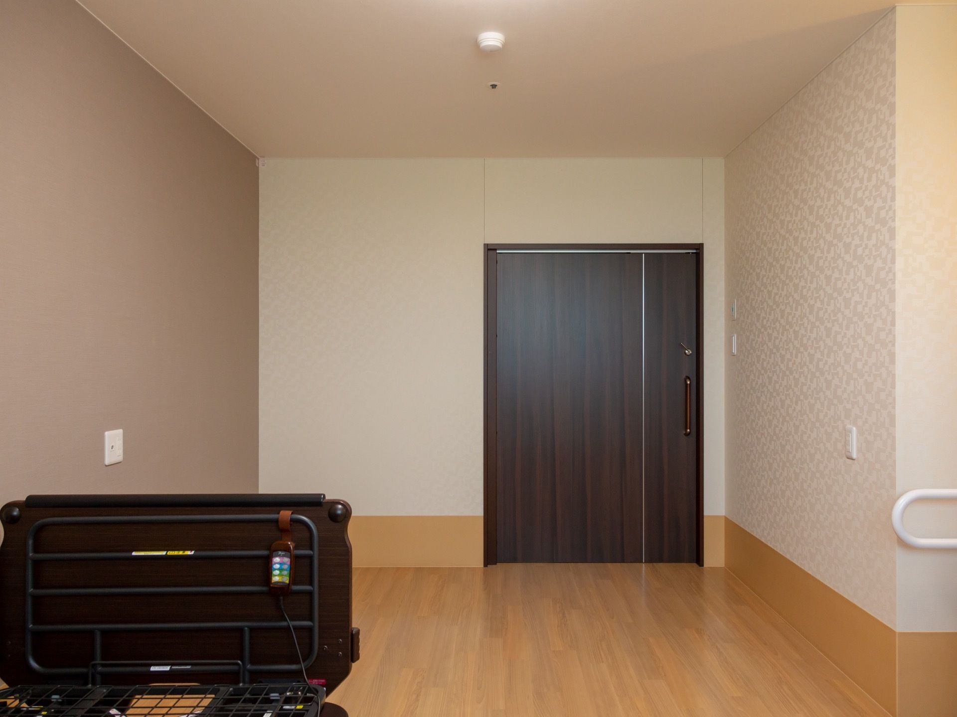 居室ドアはダークブラウンの木製ドアで引き戸式になっている。部屋の間取りはほぼ四角に近く、床はフローリングになっている。