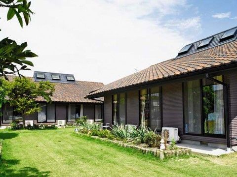 木造平屋建ての住宅。瓦葺の落ち着いた趣の屋根が特徴的である。一軒家のような外観で温かみがある。広い庭は芝生が青々と茂っている。