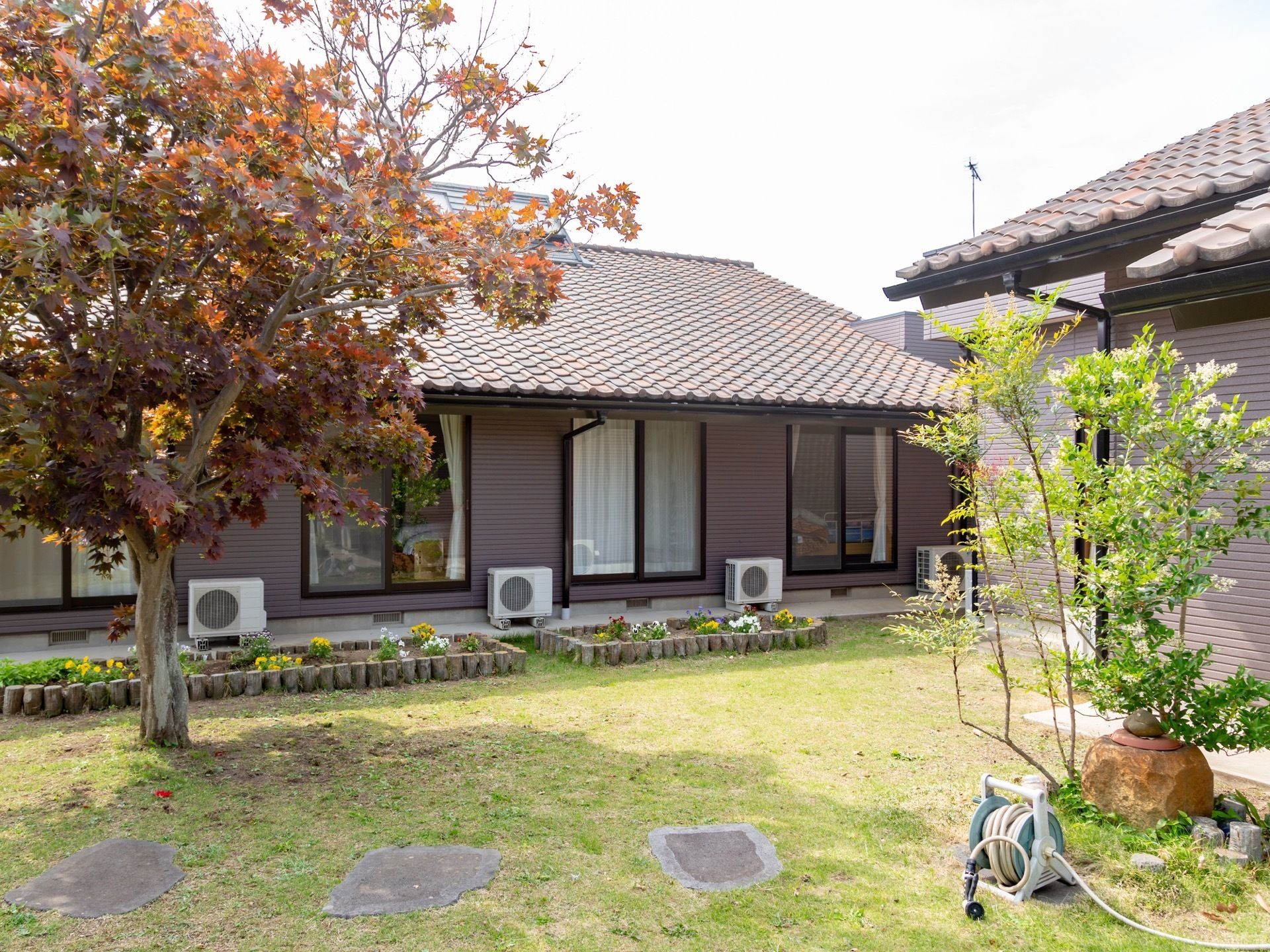 芝生が敷かれた庭が木造平屋建ての建物裏手に設けられている。花壇が設置されており、数種類の気が植えられている。