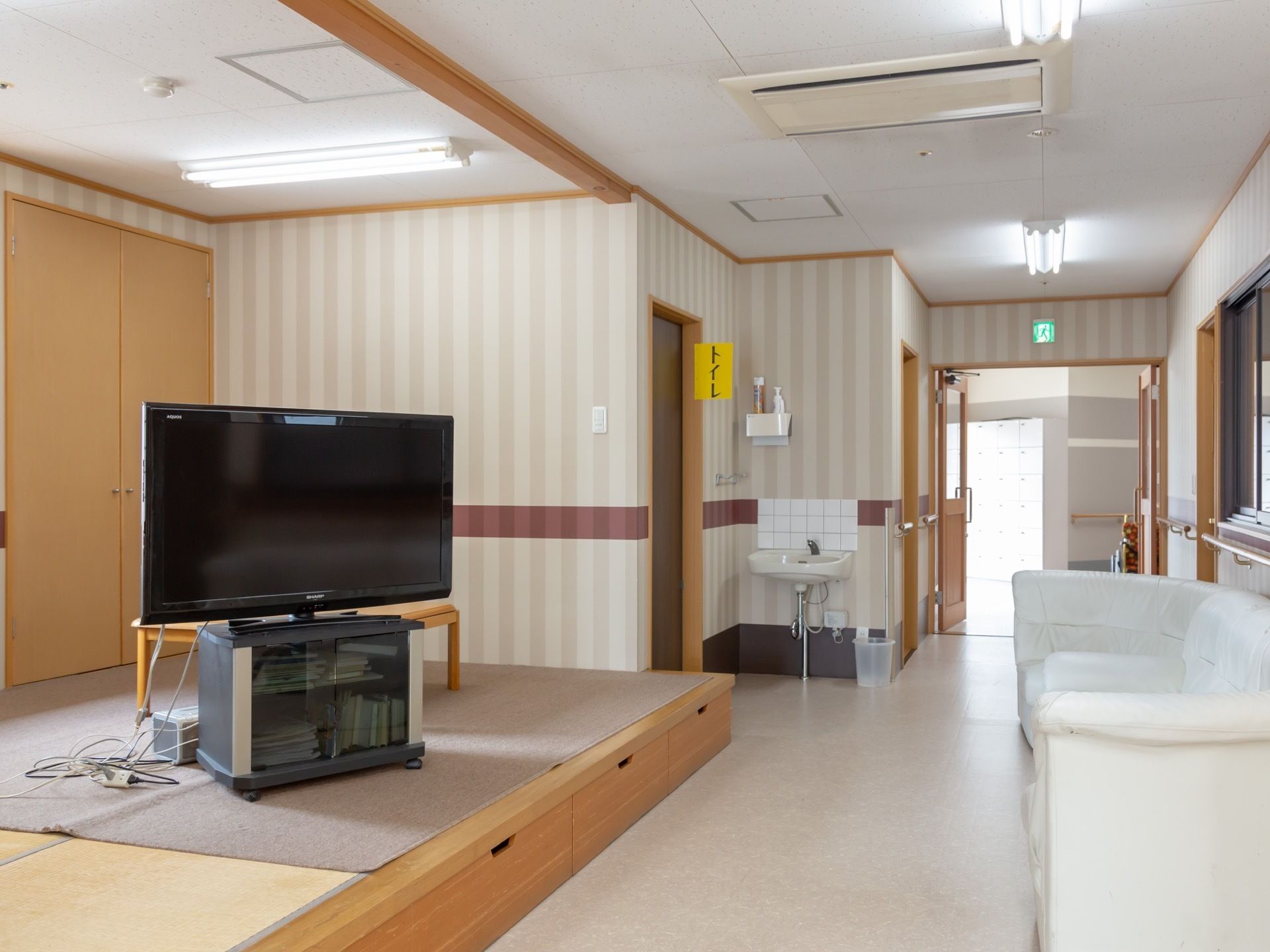リビングに設けられた和室には、テレビが設置されている。ソファが向かいの壁際に置かれている。トイレ近くの壁には、洗面台がある。