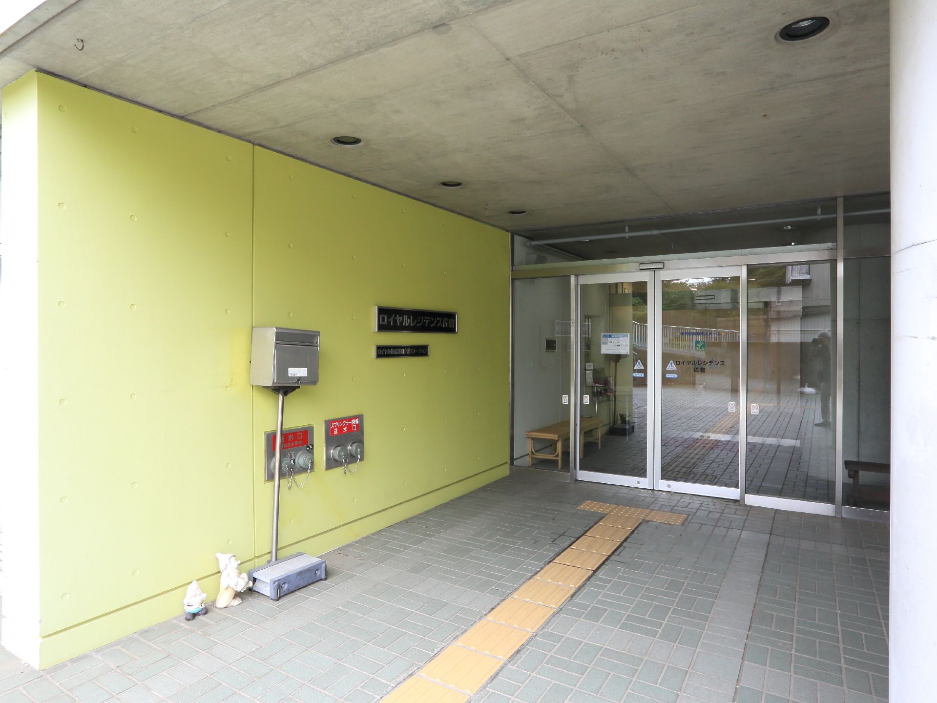 施設入口付近は黄色い壁になっている。その前にはポストが置かれ、小人の置物が飾られている。入り口は自動ドアになっている。