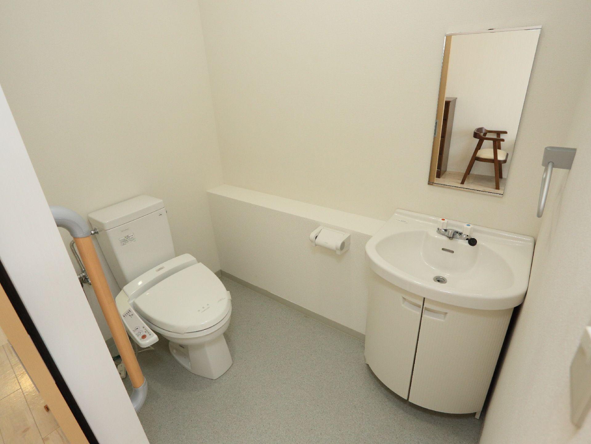 トイレと収納スペース付洗面台が併設されている広々としたスペース。鏡、タオルハンガーが取り付けられている。