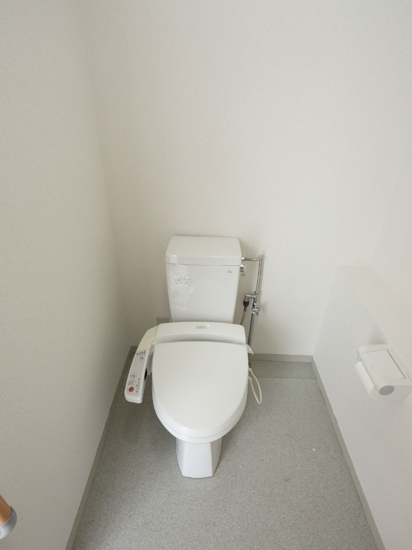 白の壁とグレーの床のシンプルな雰囲気のトイレ。車椅子の方もストレスなく使用できる広いスペースがある。