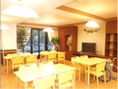 壁際にテレビがあり、テーブルと椅子、車椅子が置いてあるリビング