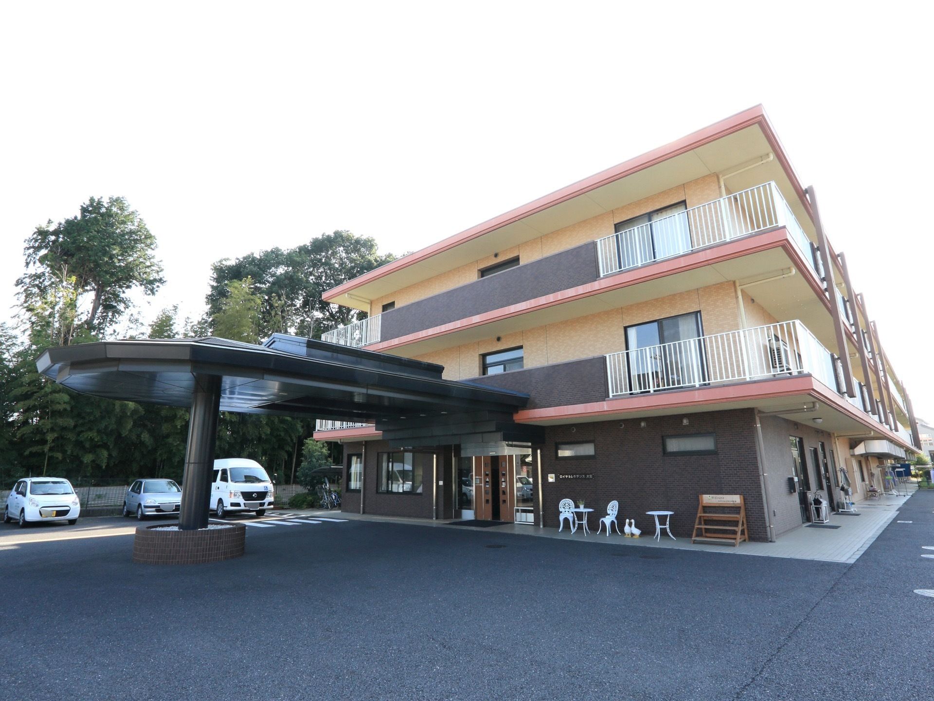 施設の外側部分には広いスペースが取られており、一面舗装道路となっている。奥には何台かの車が停まっている。