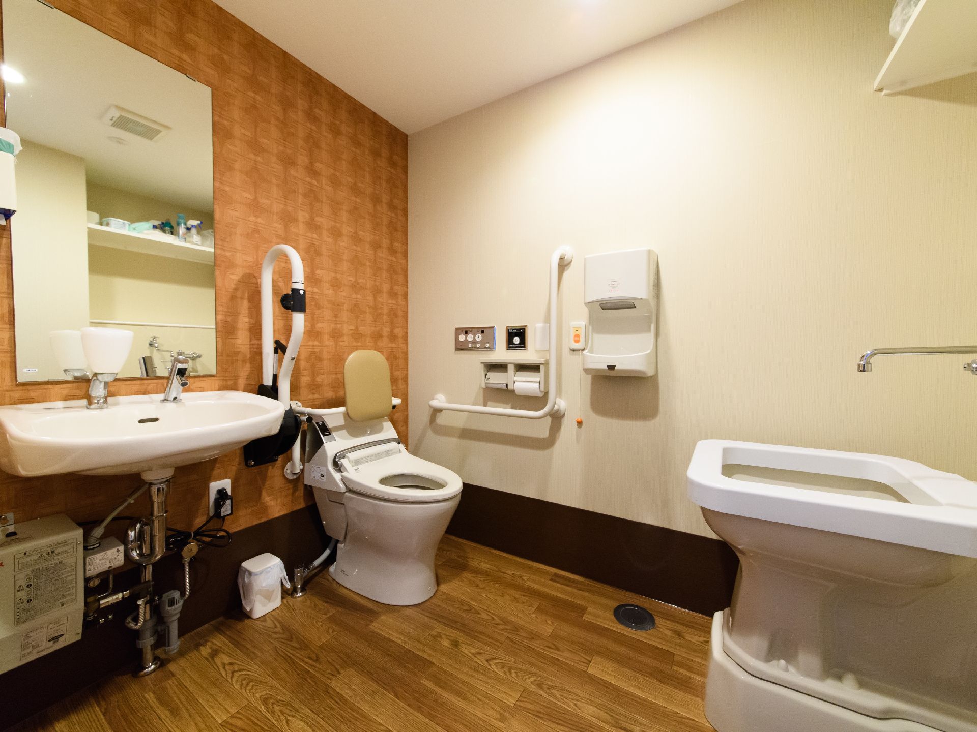トイレルームにある便座には、背もたれがついている。手洗い場は2ヶ所あり、手を乾かす温風機も設置されている。