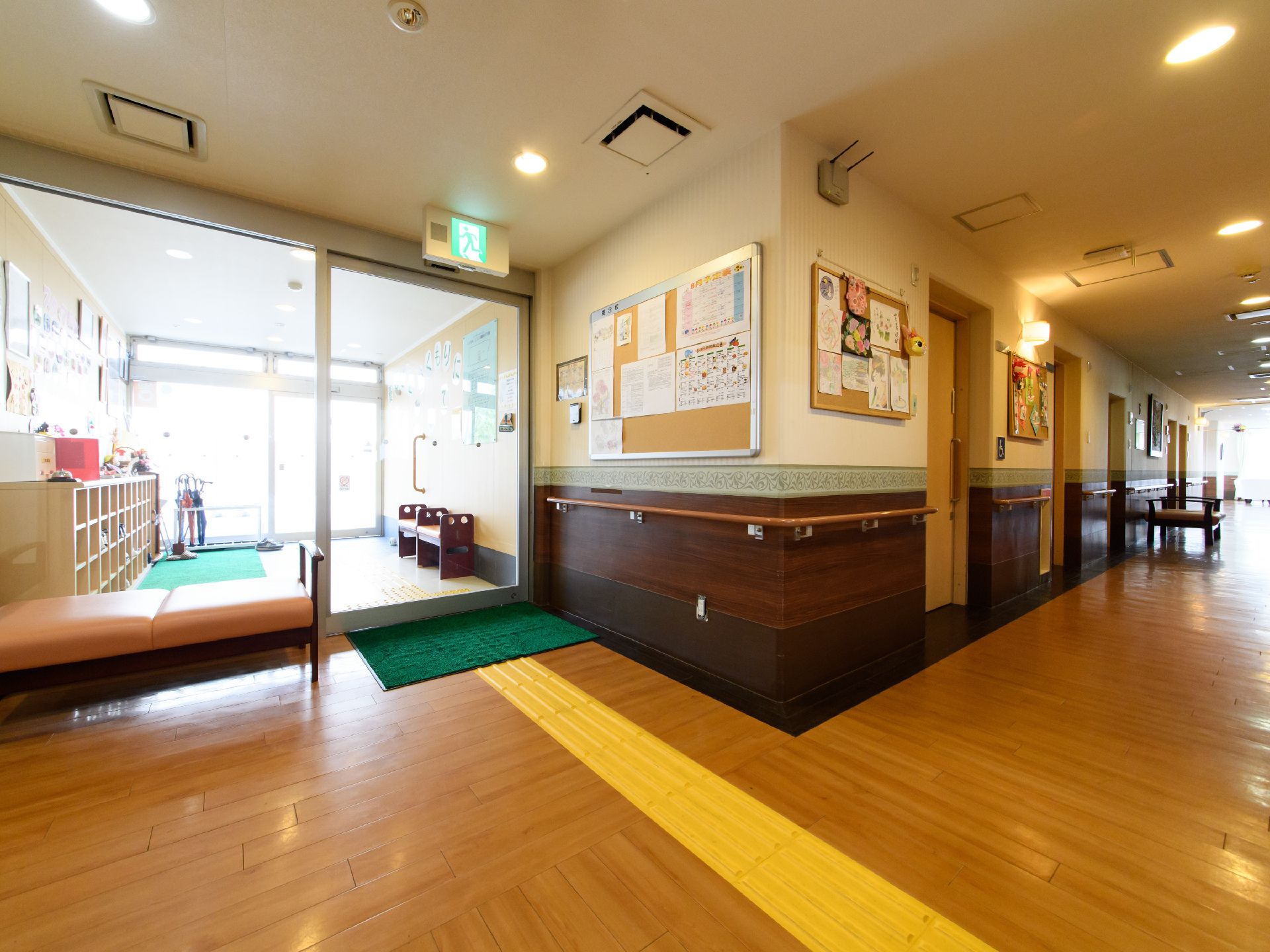 エントランスから廊下が広がっており、壁には手すりといくつかのドアが設置されている。奥にはイスも見える。
