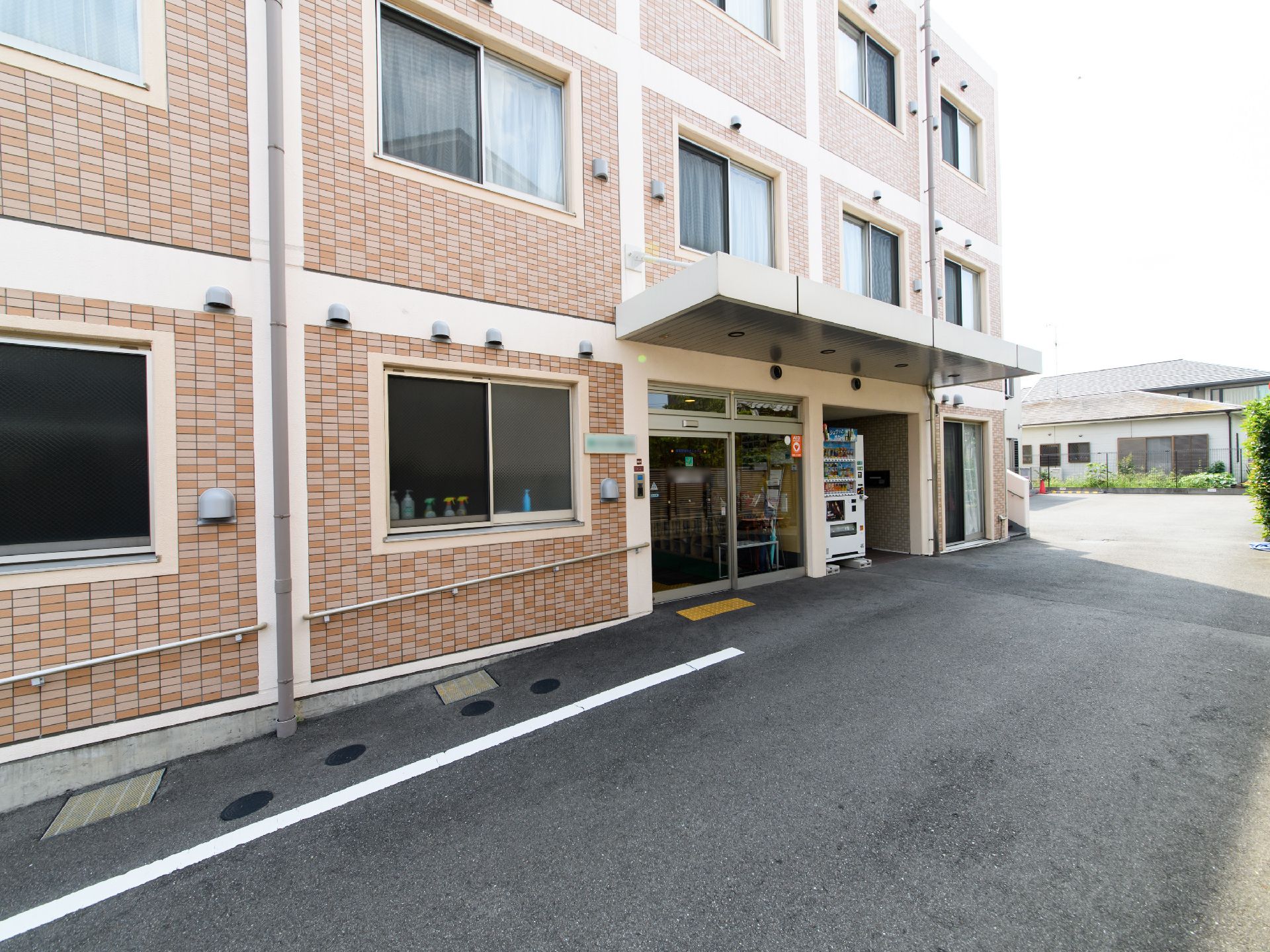 施設入口の左側の外壁に沿って、ゆるやかな傾斜になっている。外壁には手すりが取り付けられている。入口横の外壁には施設名の書かれた表札がある。