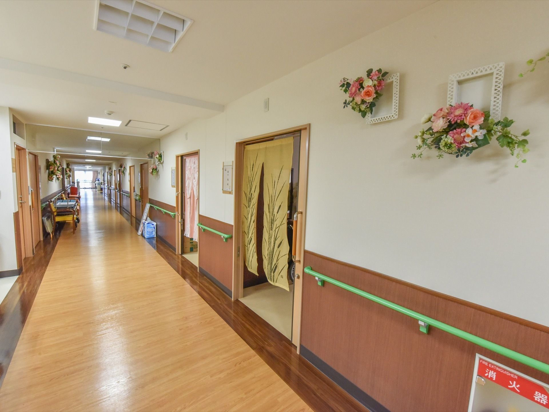 廊下の壁にはリースなど花をあしらった飾りが多く飾られている。足元の半透明の蓋には消火器が収まっている。