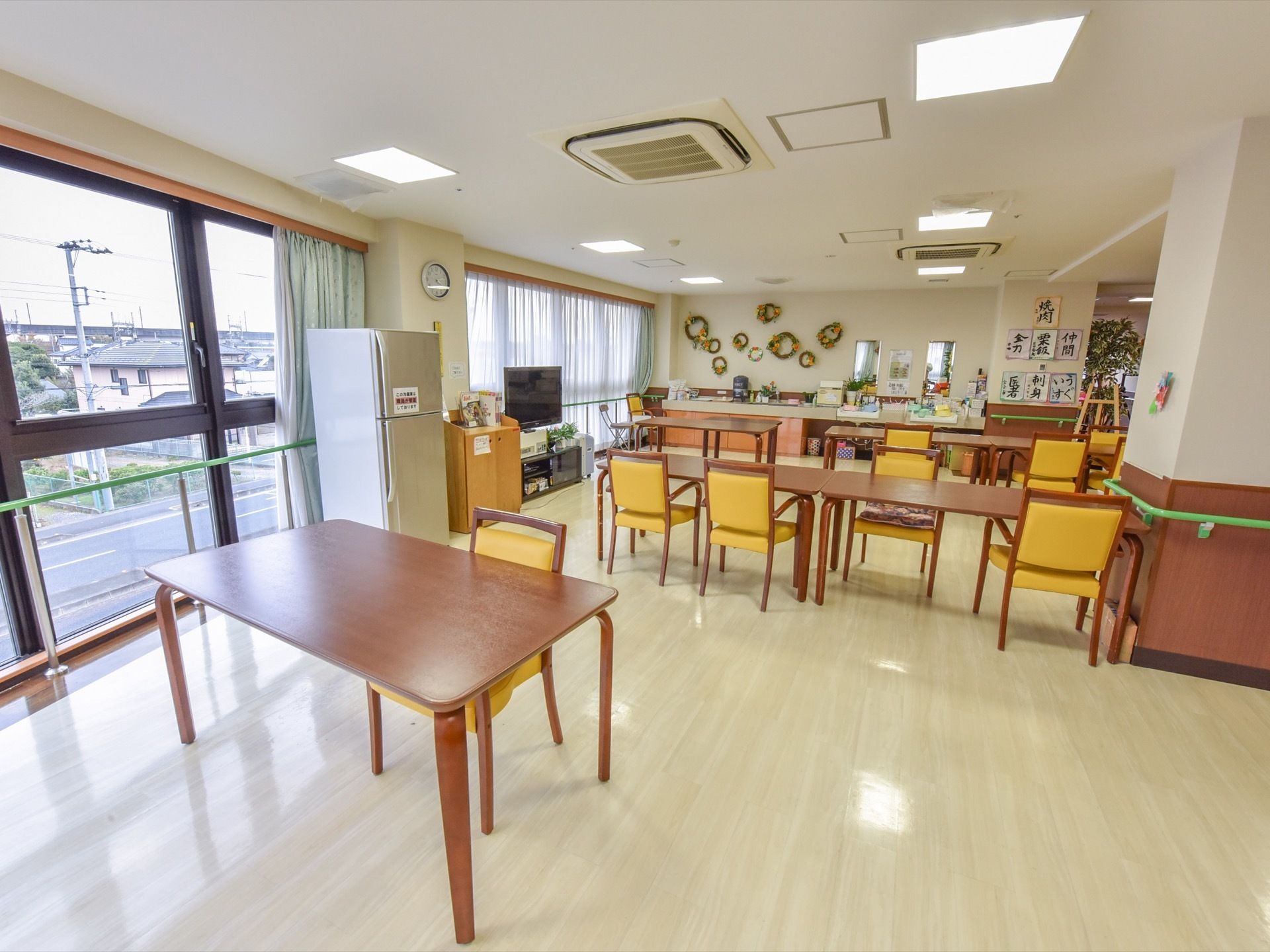 広々としたスペースの食堂になっており、奥には洗面台がある。壁には入居者様の書道の作品やリースが飾られ、明るい雰囲気になっている。