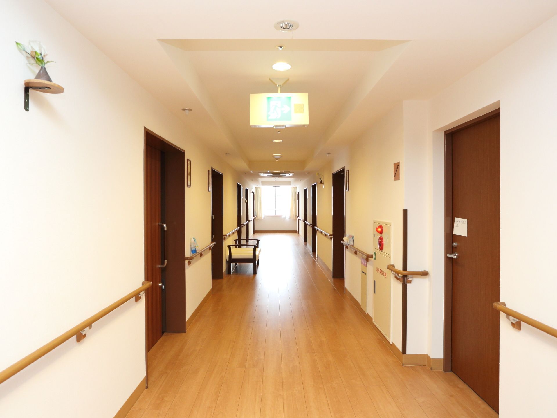 居室前の廊下はフローリングで、壁には手すりが設置してあるので、歩行がしやすくなっている。廊下に椅子が置いてある。ハンドルドアがついている。