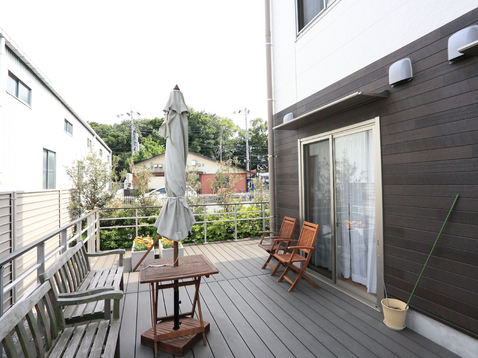 植栽がしてありフェンスで囲まれたウッドデッキには、ベンチ、チェアが置いてあり、日陰を作るパラソルも設けてある。