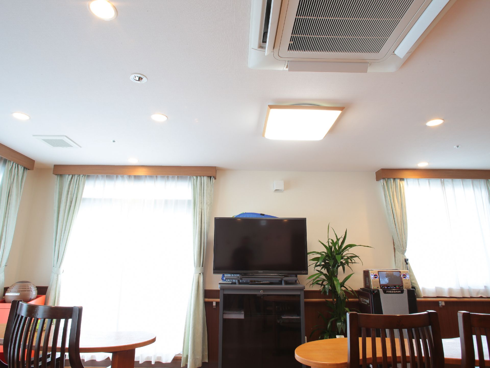 窓が多く明るい部屋に置かれた壁際のテレビとカラオケセット