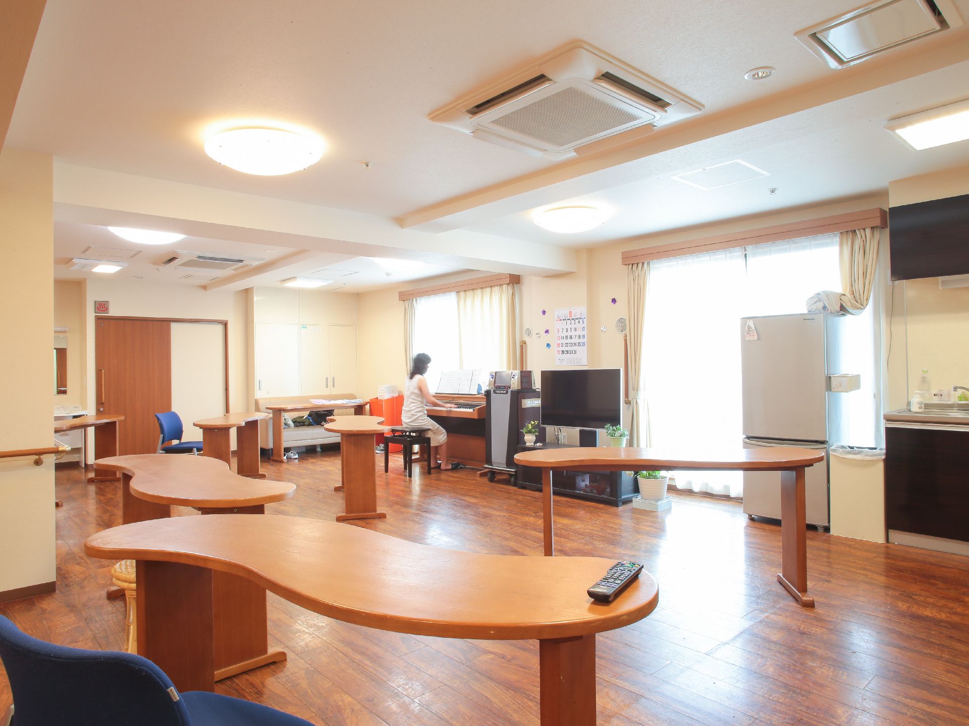 ピアノ、テレビ、冷蔵庫がある。たくさんのテーブルが置かれている。窓があり、とても明るい空間となっている。