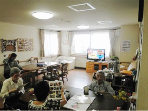 リビングルームのテーブル席では、入居者様が思い思いの時間を過ごしている。２面に窓があり、自然光が入ってくる。