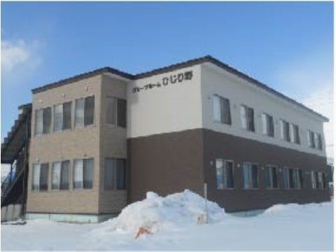 雪の中に建つ２階建てコンクリート素材の建物で、外壁には薄いベージュ、茶色、白が使われている。窓が多く付いており、日差しも十分差し込んでいる。