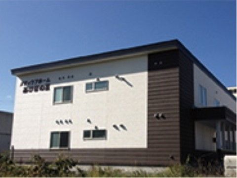 二階建ての建物が見える。施設が大きく書かれた看板が壁に掲示されている。施設の周りには植物が植えられている。