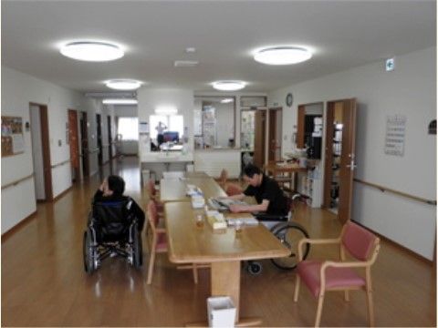 中央にテーブルが置かれており、椅子がいくつかある。二人の入居者様が写っている。手洗い場が設けられている。