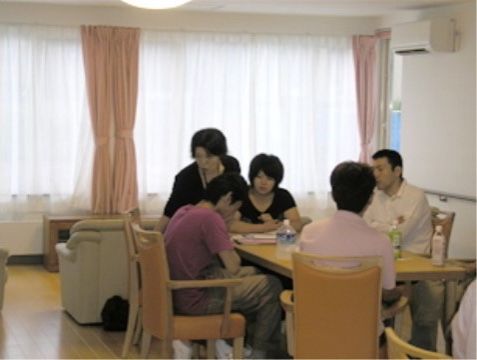 窓が大きく日当たりも良好で、木製のテーブルセットが設置されていて、入居者様同士が交流できる場所で、ソファーも設置されている。
