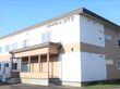施設は2階建てで窓がたくさんある。敷地内には車の駐車スペースが設けられている。周りには雪景色が広がっている。