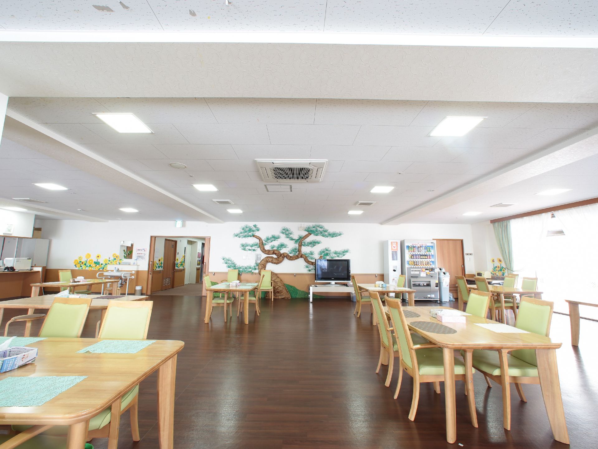 壁にはヒマワリの絵が飾ってある華やかな食堂には、木製のテーブル、椅子やスツールが置いてある。左手奥にカウンターがあり厨房になっている。