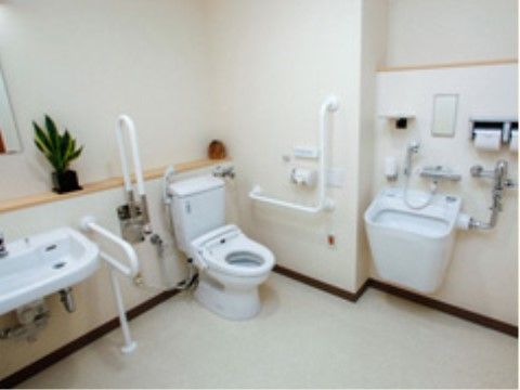 白が基調になっている広めのトイレ。洗面台がすぐ横にあり、Ｌ字型やＵ字型の白い手すりが複数設置されている。