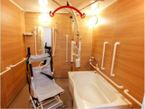 木の壁の浴室で、白い浴槽が右の壁際にある。３方向の壁に縦向きや横向きの手すりがいくつも設置されている。