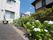 施設の建物は2階建てで、各階に窓が設けられている。前面には植物が植えられており、手前には白い花が咲いている。