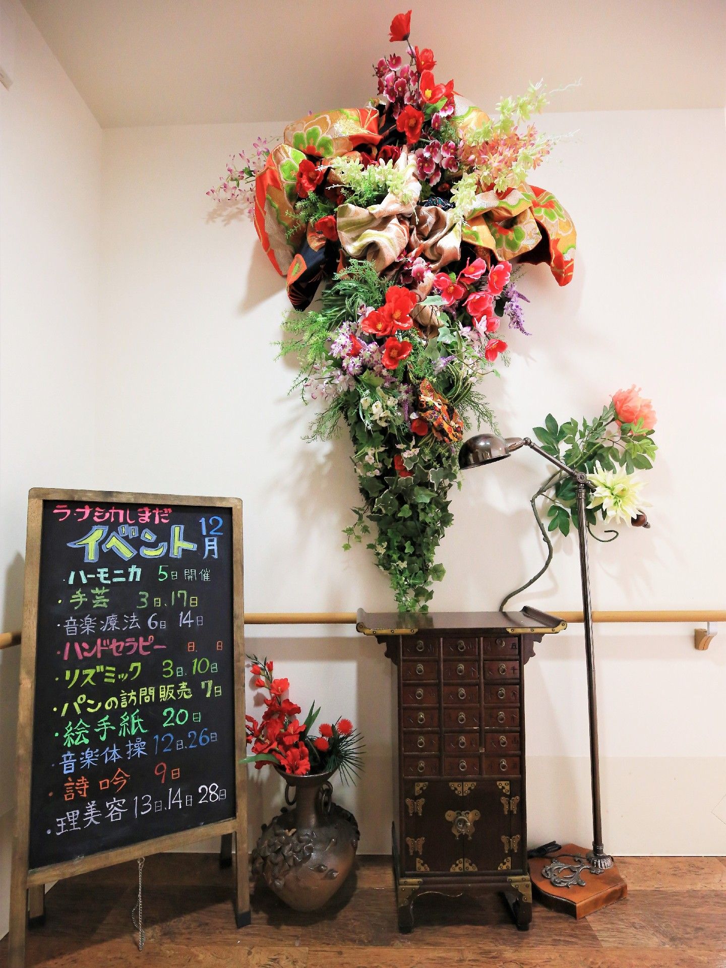 大きな花束が掛けられている一角。飾り棚と花瓶が飾られている。イベントの告知が書かれたボードが置かれている。