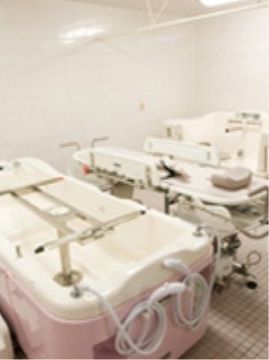 タイプが異なる特殊介助浴槽が２台並んでいる。手前には電動リフトで横になったまま浴槽まで移動できるストレチャーがある。
