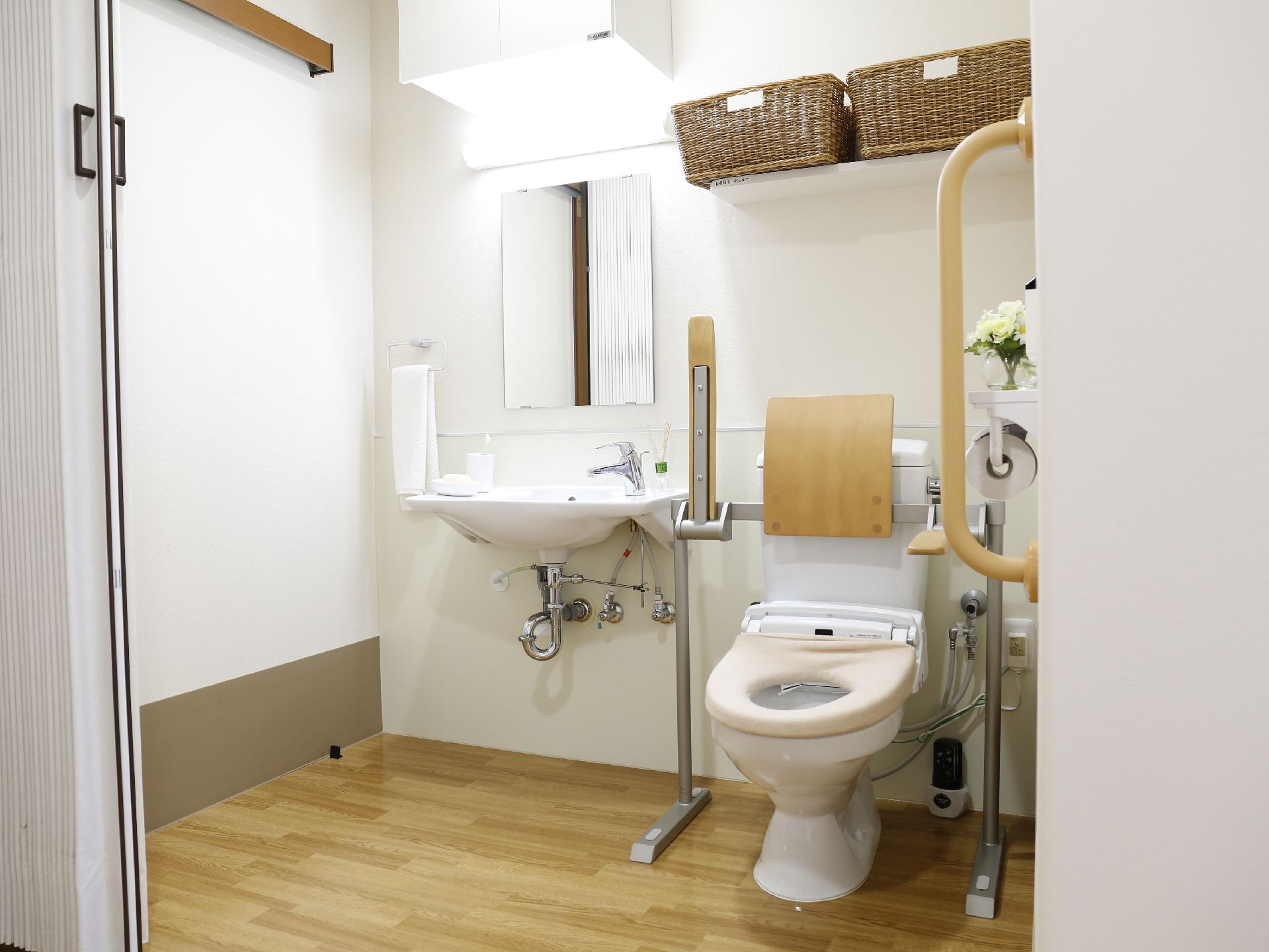じゃばらの扉を開けると広い空間のトイレと洗面台がある。トイレの脇にてすりがついており車いすでもストレスなく利用が可能である。