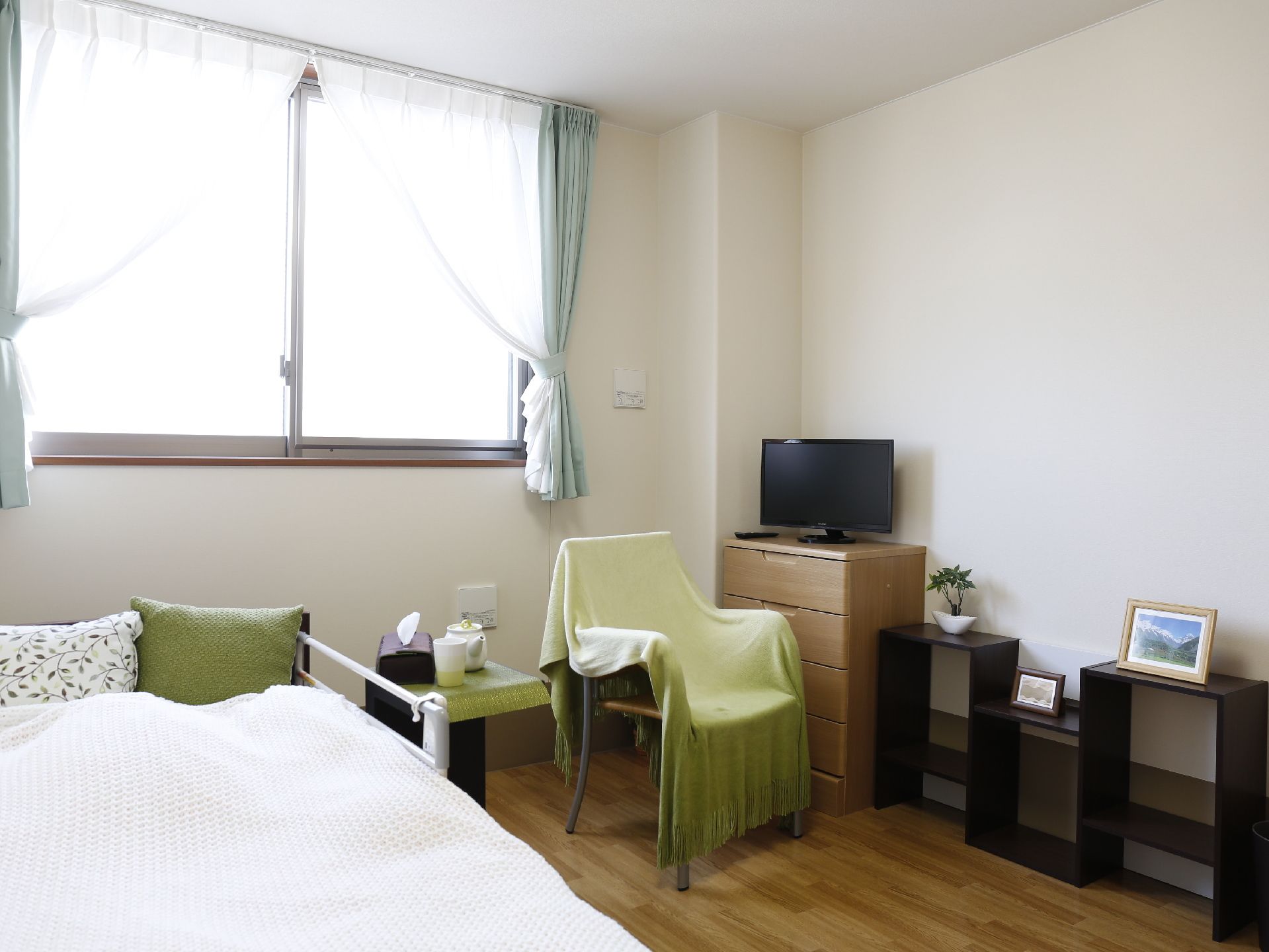 光を取り入れる大きな窓がある。部屋には利用者の持ち物を収納する棚や椅子、ベッドなどが設置されている。
