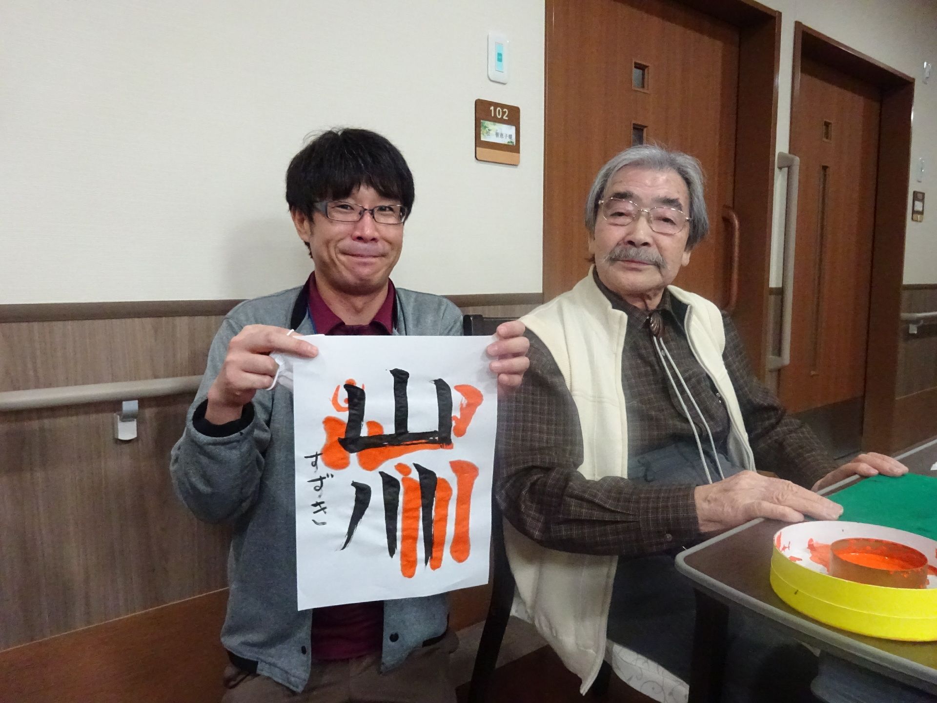入居者様が書き上げた習字の半紙を、隣で手にしている男性スタッフ