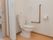 トイレの様子。手洗い付きのトイレで、壁にＬ字型の手すりが設置されている。タオルハンガーが設置されている。