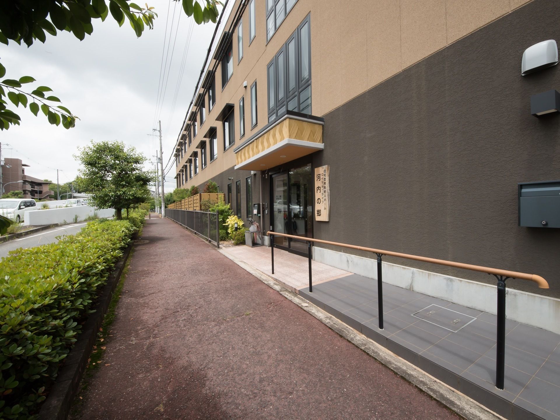 建物の玄関付近。自動ドアの上にはひさしが張り出しており、右側には施設名の入った木製の大きな看板がある。