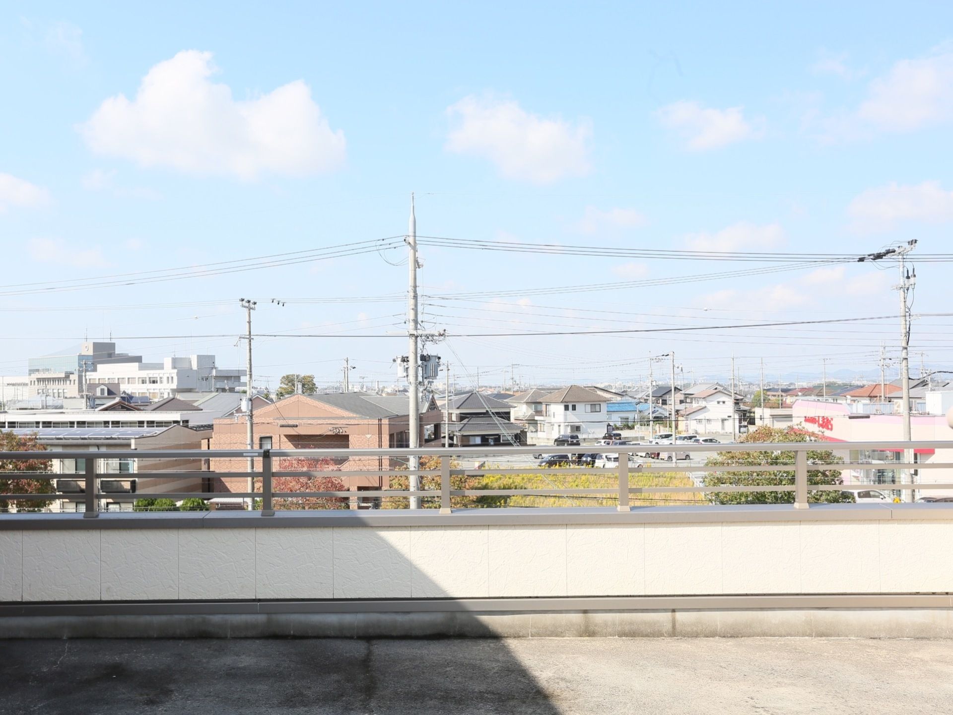 左手に見える白いビル以外は、２階建て程度の住宅が広がる、のどかな地域である。随所に見える電柱が住宅街から突きだす高さとなっている。